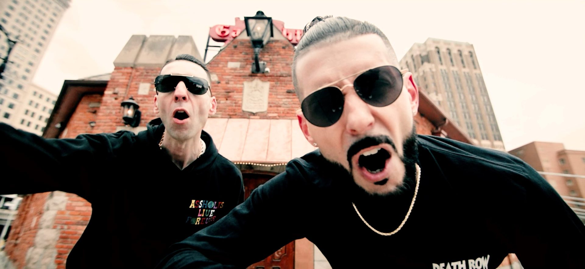 KING T and LUSS in sunglasses yelling at the camera in front of a Detroit brick building